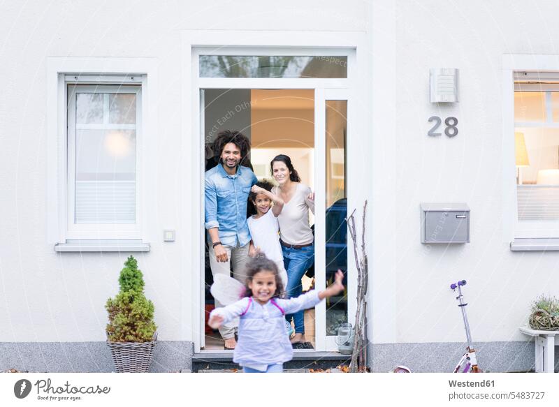 Lachende Familie wartet am Eingang ihres Hauses Familien Eigenheim Eigenheime wohnen stehen stehend steht Willkommen Eingangstür Eingangstuer Eingangstüren