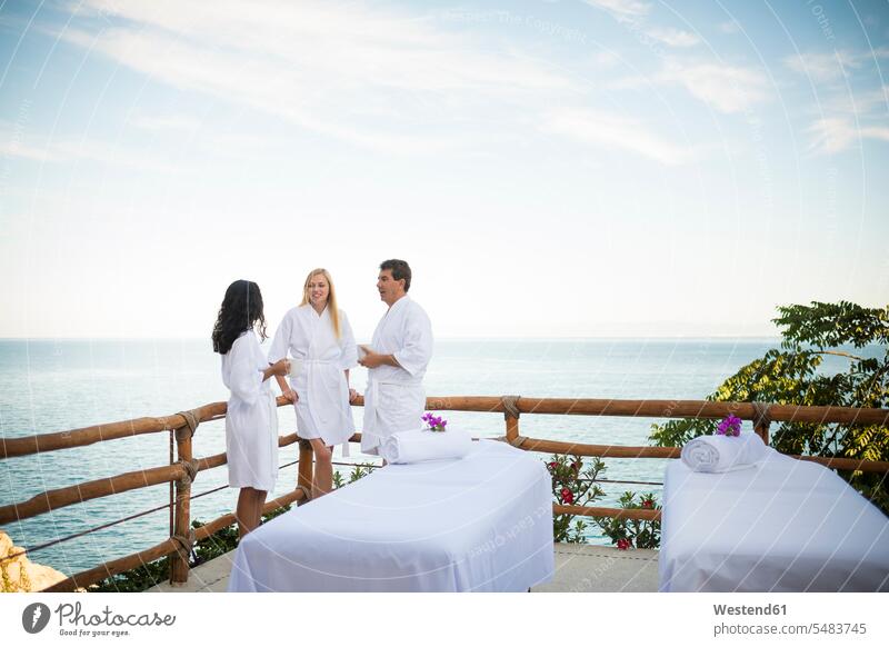 Feriengäste, die auf ihre Massage im Freien auf der Terrasse eines Luxusferienortes am Meer warten Bademantel Bademäntel Wellness Gesundheit Urlaub Tourismus