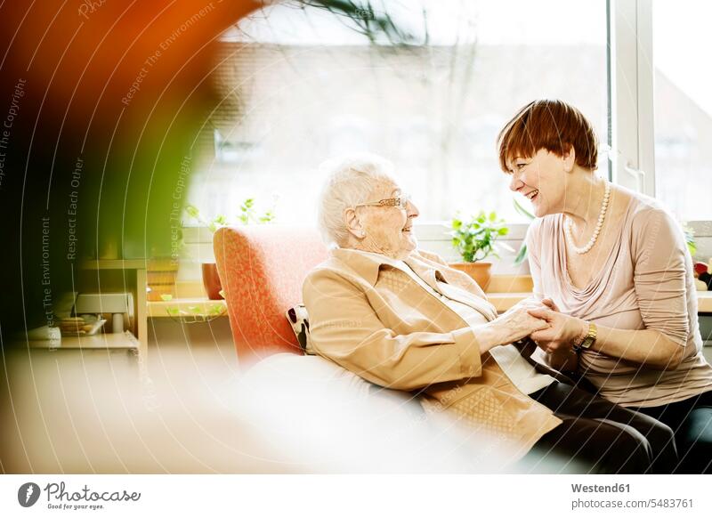 Erwachsene Tochter im Gespräch mit ihrer Mutter mit Alzheimer-Krankheit in ihrem Zimmer im Altenheim Erwachsene Töchter Betreuung betreuen besuchen Besuch