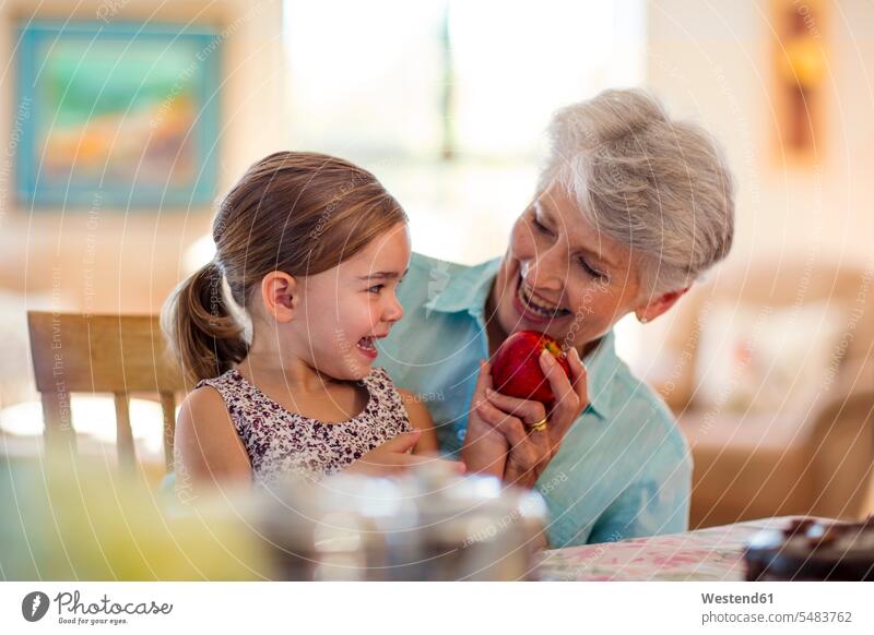 Enkelin sitzt auf dem Schoss der Grossmutter und hält einen Apfel essen essend lachen Äpfel Aepfel Enkeltochter Enkelinnen Enkeltöchter Großmutter Oma Grossmama