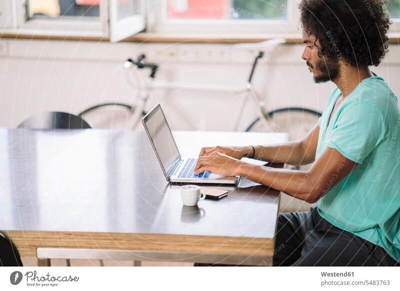 Junger Mann im Büro mit Laptop arbeiten Arbeit Designer sitzen sitzend sitzt jung Office Büros Notebook Laptops Notebooks Arbeitsplatz Arbeitsstätte