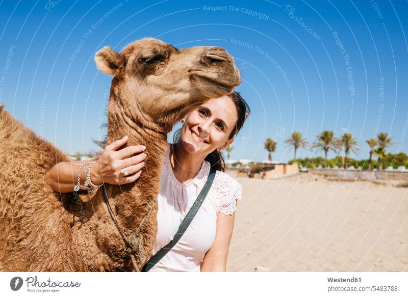 Marokko, Tanger, Porträt einer lächelnden Frau mit Babykamel am Strand Portrait Porträts Portraits Beach Straende Strände Beaches Kamel Kamele weiblich Frauen