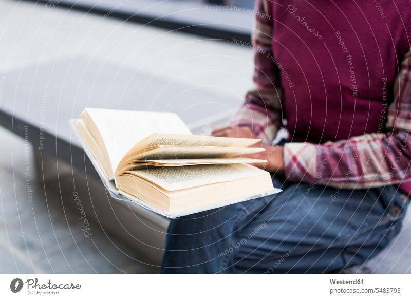 Mann sitzt auf Bank und liest ein Buch, Teilansicht lesen Lektüre Bücher Sitzbänke Bänke Sitzbank Student Hochschueler Studierender Hochschüler Studenten