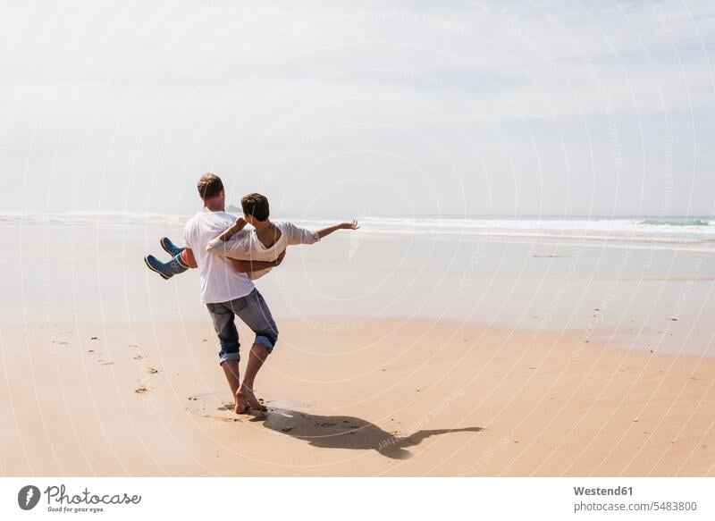 Erwachsener Mann trägt seine Frau am Strand Paar Pärchen Paare Partnerschaft tragen transportieren Urlaub Ferien glücklich Glück glücklich sein glücklichsein
