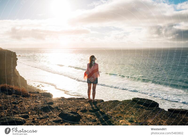 Spanien, Fuerteventura, El Cotillo, Rückenansicht einer Frau, die bei Sonnenuntergang zum Meer schaut hell Tuch Tuecher Tücher Halstuch Schal Halstuecher Schals