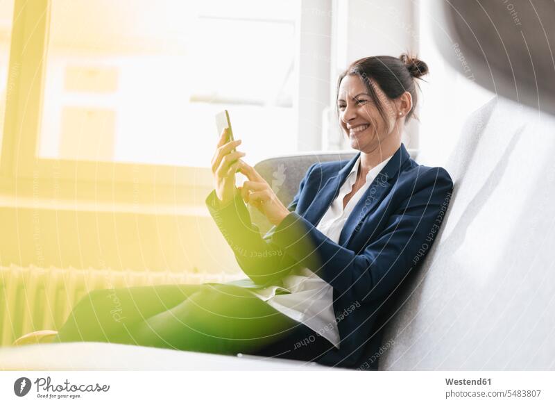 Lachende Geschäftsfrau, die mit ihrem Handy auf einer Couch sitzt Geschäftsfrauen Businesswomen Businessfrauen Businesswoman Selfie Selfies Frau weiblich Frauen