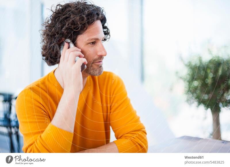 Mann mit lockigem braunen Haar telefoniert mit Smartphone Männer männlich telefonieren anrufen Anruf telephonieren iPhone Smartphones Erwachsener erwachsen