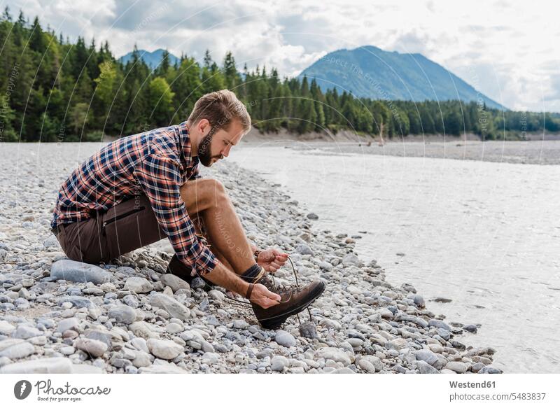 Deutschland, Bayern, Wanderer sitzt am Flussufer und bindet sich den Schuh Mann Männer männlich Erwachsener erwachsen Mensch Menschen Leute People Personen