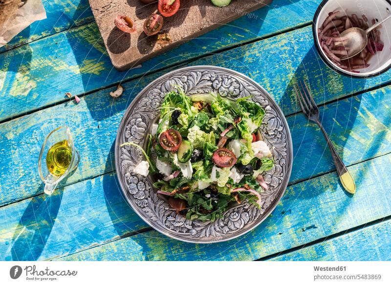 Griechischer Salat mit Rucola, Käse, Oliven, Tomaten, Gurken, Zwiebeln und karamellisierten Nüssen Teller Holz hoelzern hölzern Gesunde Ernährung Ernaehrung