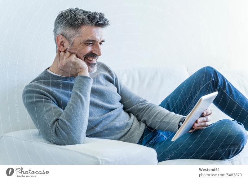 Lächelnder reifer Mann zu Hause mit Tablette Sofa Couches Liege Sofas Männer männlich Tablet Computer Tablet-PC Tablet PC iPad Tablet-Computer Erwachsener