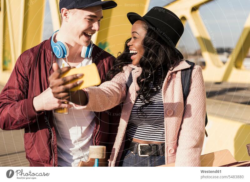 Junges Paar geht auf der Brücke und benutzt ein Smartphone fröhlich Fröhlichkeit Frohsinn Heiterkeit jung lachen multikulturell Pärchen Paare Partnerschaft