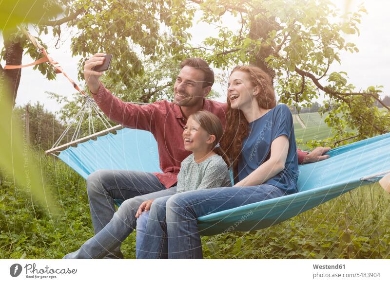 Glückliche Familie sitzt in der Hängematte und macht ein Selfie Garten Gärten Gaerten Tochter Töchter Handy Mobiltelefon Handies Handys Mobiltelefone Selfies