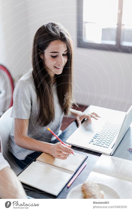 Lächelnde Frau zu Hause am Laptop und macht sich Notizen Zuhause lächeln notieren Computer Freiberufler WLan Beruf Laptop benutzen Tisch Häusliches Leben sitzen