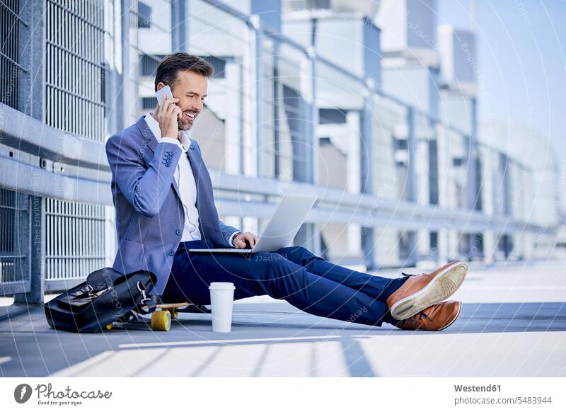 Geschäftsmann telefoniert und benutzt Laptop im Freien lächeln telefonieren anrufen Anruf telephonieren sitzen sitzend sitzt Skateboard Rollbretter Skateboards