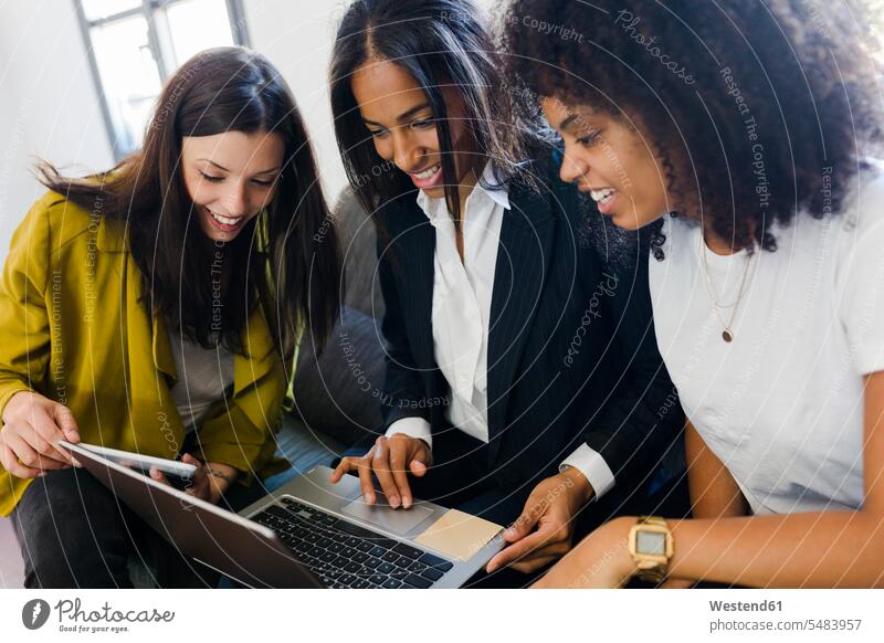 Drei lächelnde Geschäftsfrauen teilen sich einen Laptop im Büro Office Büros Arbeitsplatz Arbeitsstätte Arbeitstelle Businesswomen Businessfrauen Businesswoman