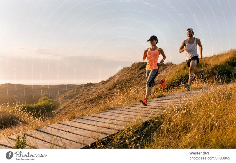 Spanien, Aviles, Athletenpaar läuft bei Sonnenuntergang einen Küstenweg entlang Paar Pärchen Paare Partnerschaft Läuferin Laeuferinnen Läuferinnen Freizeit Muße