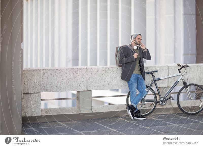 Junger Mann am Handy neben dem Fahrrad Mobiltelefon Handies Handys Mobiltelefone Männer männlich telefonieren anrufen Anruf telephonieren Telefon Kommunikation