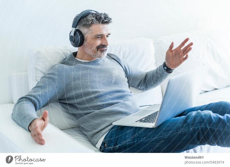 Älterer Mann zu Hause mit Laptop und Kopfhörern hören hoeren Männer männlich Notebook Laptops Notebooks Kopfhoerer Sofa Couches Liege Sofas Erwachsener