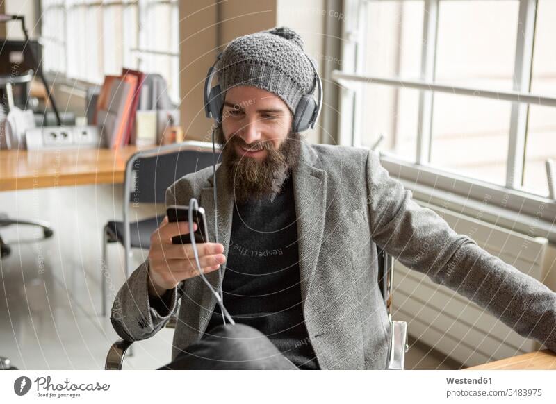 Porträt eines jungen Geschäftsmannes mit Bohnenhut und Smartphone Mann Männer männlich Hipster unkonventionell Technologie Technologien Technik Business