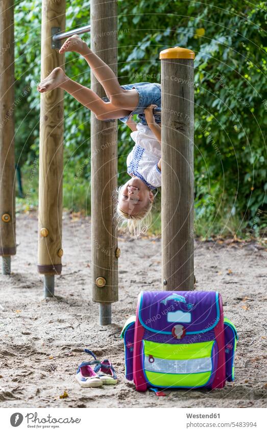Lächelndes kleines Mädchen mit Schulranzen auf dem Reck eines Spielplatzes Kind Mensch lächeln Schultasche hängen turnen Tasche Turngerät Turnen Sport Freude