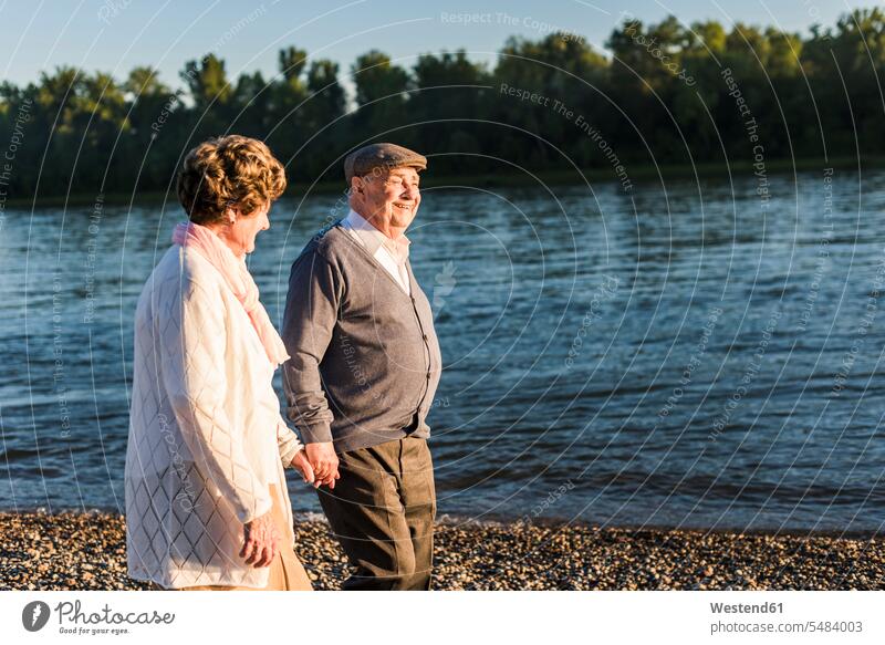 Glückliches älteres Ehepaar geht Hand in Hand am Flussufer spazierengehen Spaziergang machen spazieren gehen Seniorenpaar älteres Paar Seniorenpaare