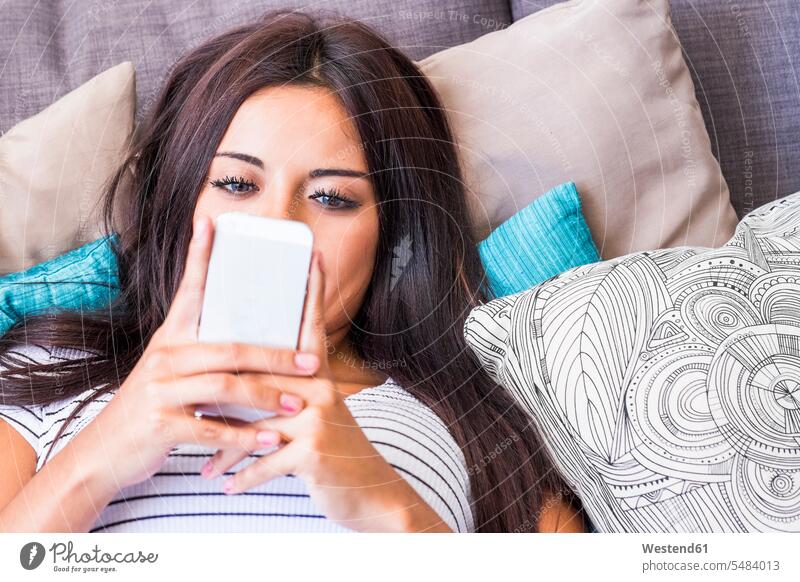 Teenager-Mädchen liegt auf der Couch und schaut auf Handy Teenagerin junges Mädchen Teenagerinnen weiblich junge Frau Smartphone iPhone Smartphones liegen