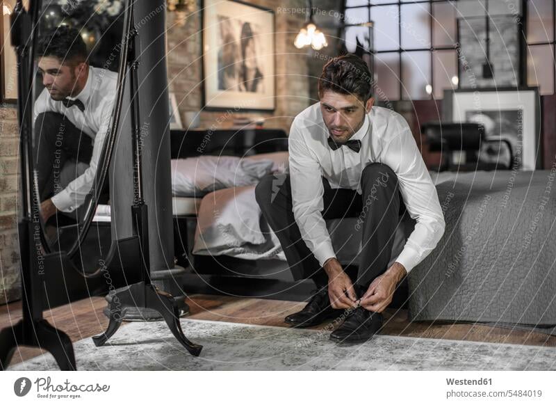 Mann sitzt auf Bett und bindet Schuhe Hemd Hemden Wohnung wohnen Wohnungen elegante Kleidung gut angezogen gespiegelt spiegeln weißes Hemd gepflegt kultiviert