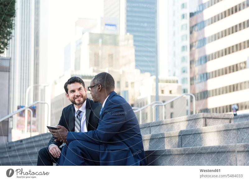 Zwei Geschäftsleute sitzen auf einer Treppe und unterhalten sich und teilen sich ein Tablett sprechen reden Geschäftsmann Businessmann Businessmänner