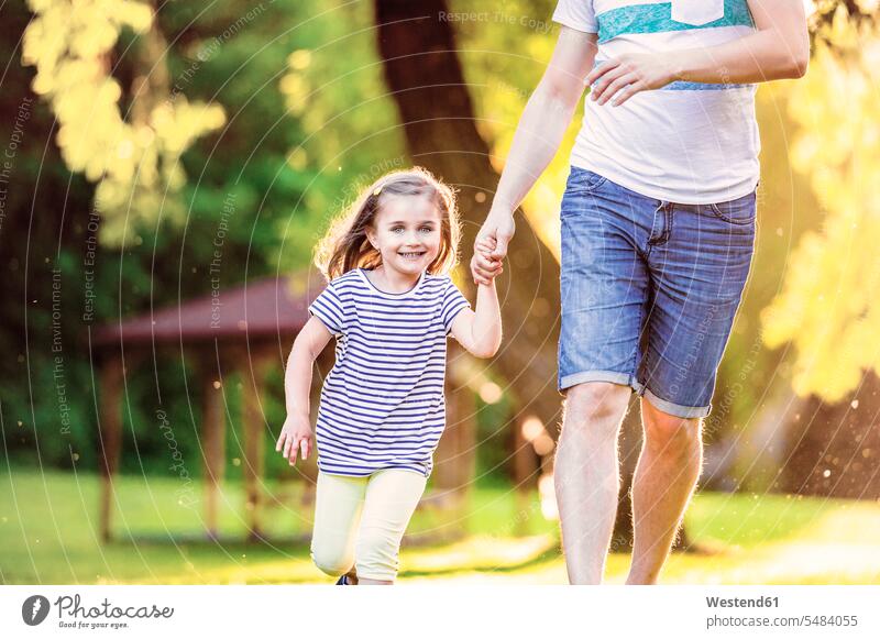 Porträt eines lächelnden kleinen Mädchens, das mit seinem Vater Hand in Hand in einem Park läuft laufen rennen Papas Väter Vati Vatis Papis Tochter Töchter