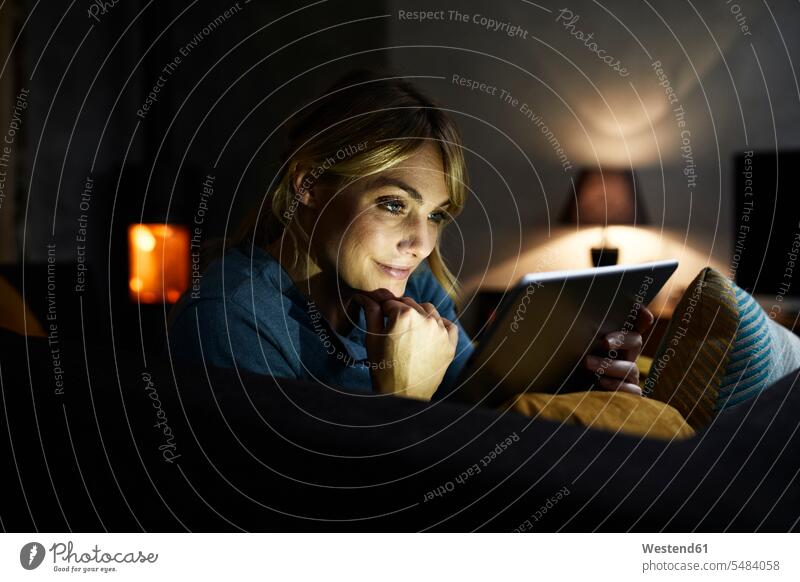 Porträt einer lächelnden Frau, die abends zu Hause auf der Couch Tabletten benutzt weiblich Frauen benutzen benützen Zuhause daheim Abend Tablet Computer