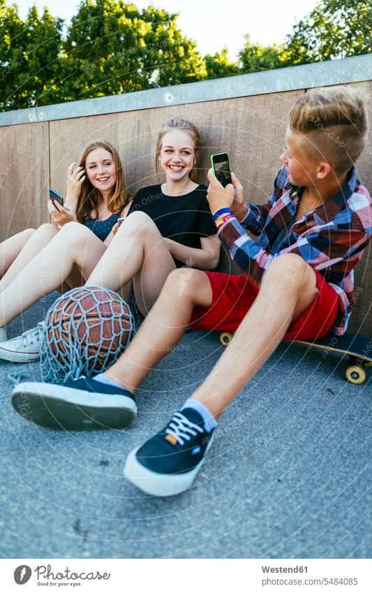 Teenager, der Freunde im Freien mit dem Handy fotografiert Skateboard Rollbretter Skateboards Außenaufnahme draußen Smartphone iPhone Smartphones Ball Bälle