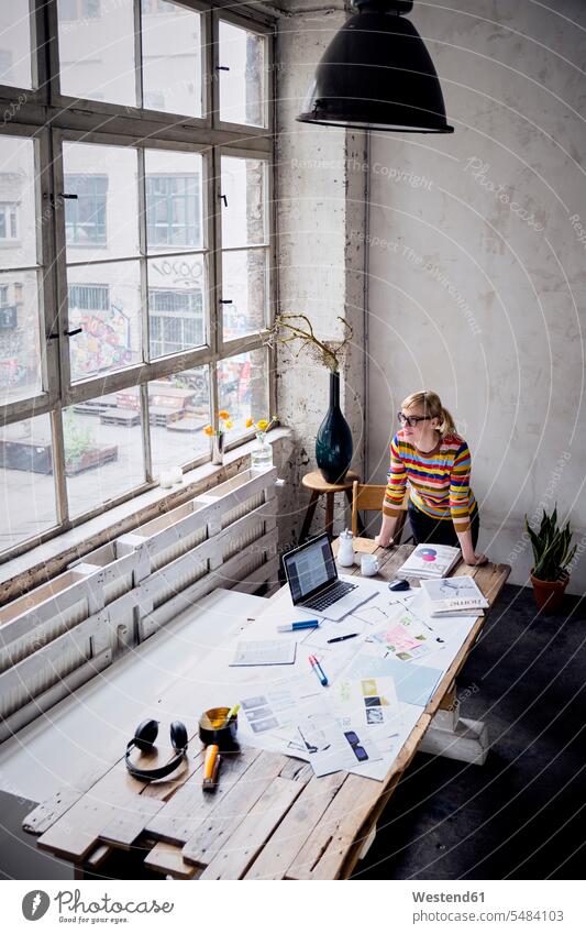 Frau steht am Schreibtisch in einem Loft und schaut durchs Fenster weiblich Frauen Freiberufler freiberuflich freie Berufe Lofts Erwachsener erwachsen Mensch