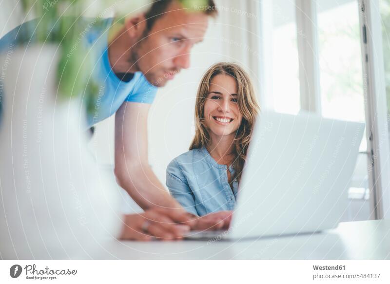 Lächelnde junge Frau und lächelnder Mann mit Laptop zu Hause Paar Pärchen Paare Partnerschaft Notebook Laptops Notebooks Home Office homeoffice zuhause