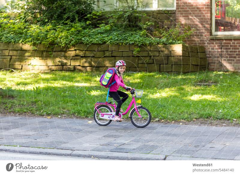 Lächelndes kleines Mädchen mit Schultasche beim Fahrradfahren auf dem Bürgersteig Gehsteig Kind Mensch Schülerin Schulkind Bildung Tasche Rad Radfahrerin