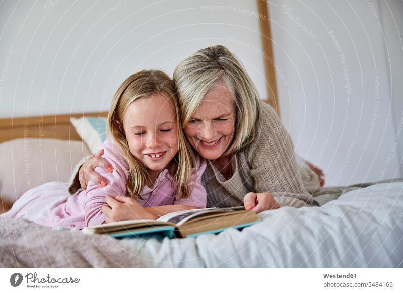 Kleines Mädchen, das mit seiner Großmutter auf dem Bett liegt und ein Buch liest Enkelin Enkeltochter Enkelinnen Enkeltöchter Betten Grossmutter Oma Grossmama
