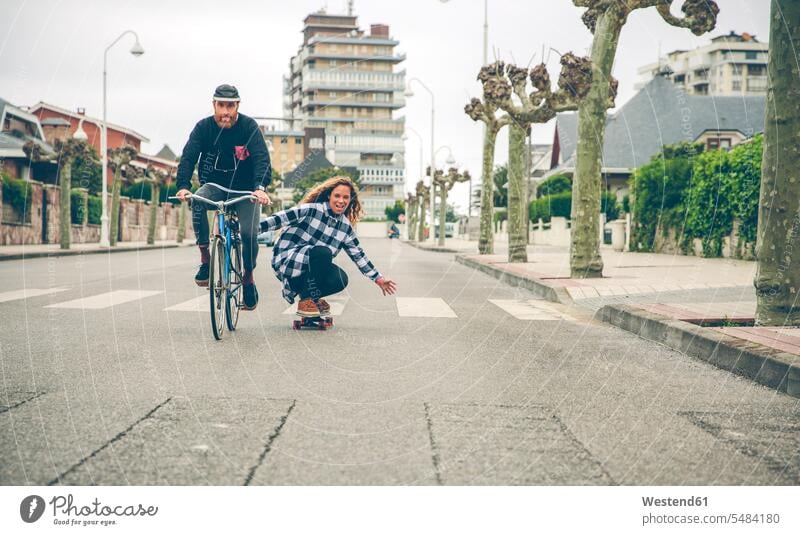 Glückliches Paar mit Fahrrad und Skateboard auf der Straße Rollbretter Skateboards Bikes Fahrräder Räder Rad fahren Strassen Straßen Pärchen Paare Partnerschaft