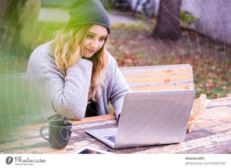 Porträt einer lächelnden jungen Frau mit Laptop, die im Herbst im Freien skyped weiblich Frauen Notebook Laptops Notebooks Portrait Porträts Portraits skypen