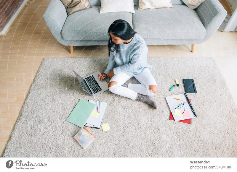 Junge Frau sitzt auf dem Boden im Wohnzimmer und benutzt einen Laptop Notebook Laptops Notebooks weiblich Frauen Computer Rechner Erwachsener erwachsen Mensch