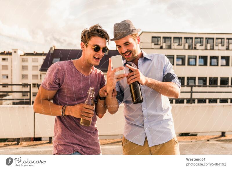 Zwei Freunde mit Bierflaschen und Handy auf dem Dach Dachterrasse Dachterrassen Mobiltelefon Handies Handys Mobiltelefone Spaß Spass Späße spassig Spässe spaßig