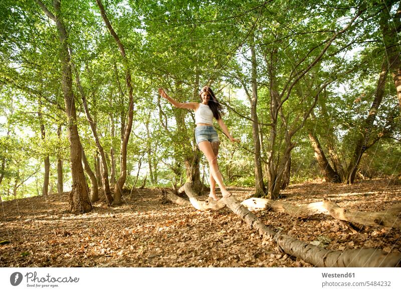 Junge Frau im Wald beim Balancieren auf einem Baumstamm Bäume Baeume weiblich Frauen lächeln Forst Wälder balancieren Balance Erwachsener erwachsen Mensch