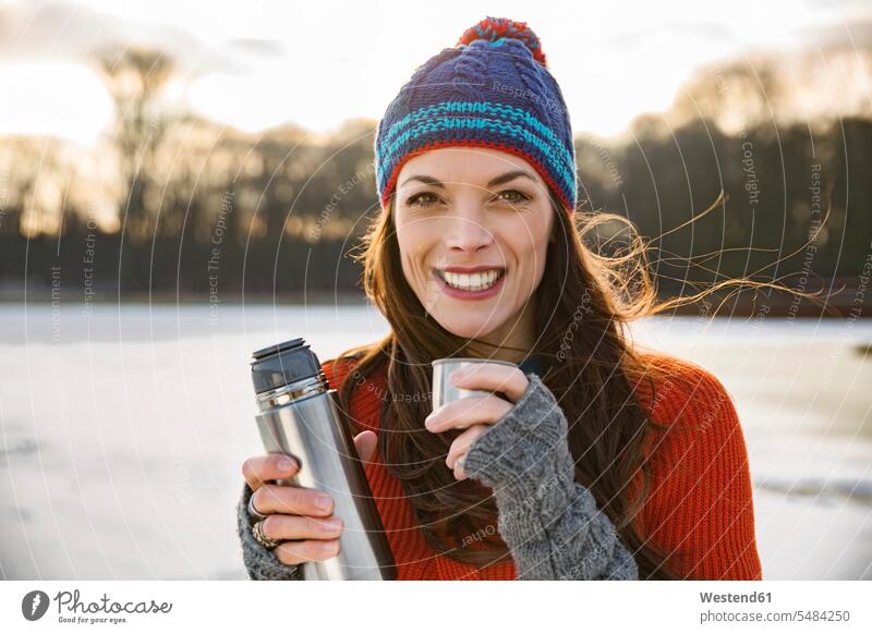 Porträt einer lächelnden Frau, die im Winter draussen im Freien Heißgetränke aus der Thermoskanne trinkt trinken Wollmütze Wollmützen Strickmütze Strickmützen
