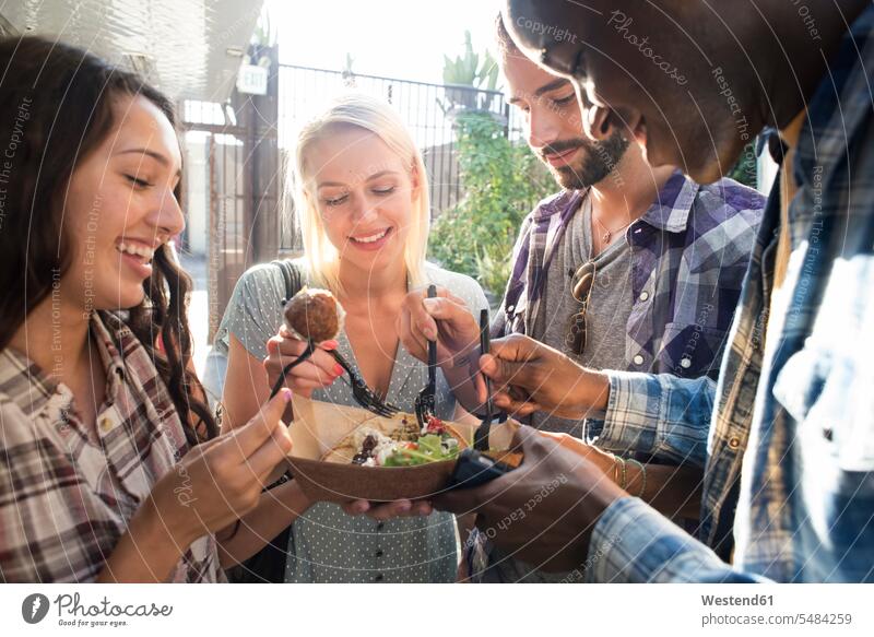 Glückliche Freunde teilen Essen zum Mitnehmen im Freien Teilen Sharing Snack Imbiss Zwischenmahlzeit Snacks lächeln essen essend Freundschaft Kameradschaft