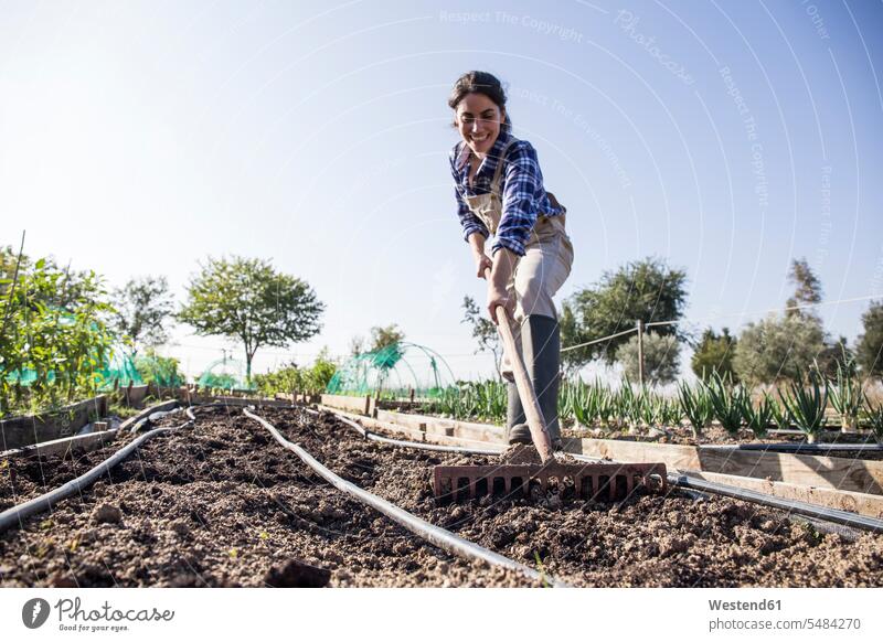 Frau arbeitet auf dem Bauernhof, bereitet Gemüsebeet mit dem Rechen vor rechen harken Gärtnerei Gaertnerei Gärtnerein Gaertnerein Bio Biologische Lebensmittel
