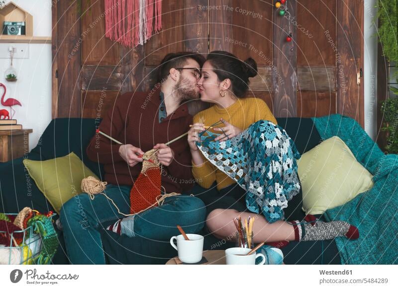 Junges Paar macht Handarbeiten und küsst sich auf der Couch Pärchen Paare Partnerschaft küssen Küsse Kuss Mensch Menschen Leute People Personen sitzen sitzend
