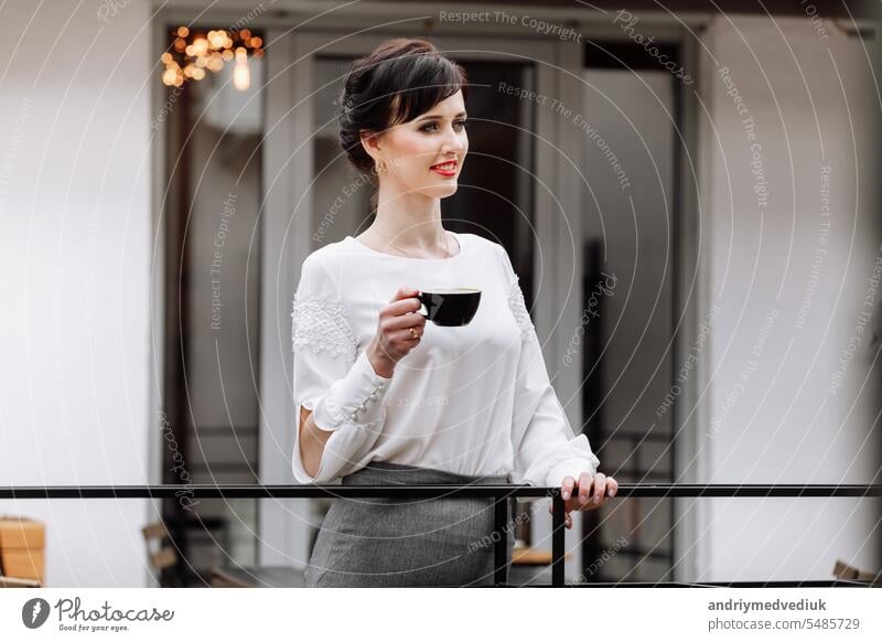 Junge schöne Frau hält eine Tasse Kaffee oder Tee im Café, Restaurant. Brunette Mädchen trinkt heiße Getränke, Blick in die Kamera im Freien auf der Terrasse und mit Mittagspause während der Arbeit. copy space