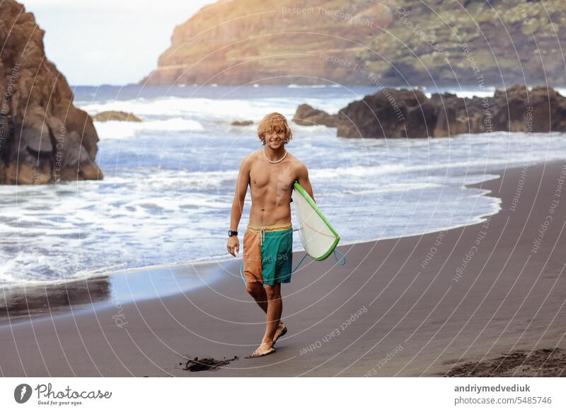 Fit jungen Surfer Mann mit lockigem blondem Haar mit Surfbrett geht durch den Ozean Spaß haben extreme Wassersportarten, Surfen. Reisen und gesunden Lebensstil Konzept. Sport Reiseziel.