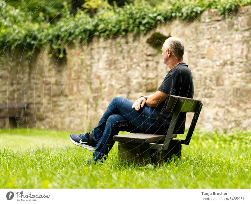 Mann mittleren Alters sitzt auf einer Parkbank mit abgewandtem Blick in die Ferne Ein Mann allein reifer Mann Erwachsener Mann mittleren Alters