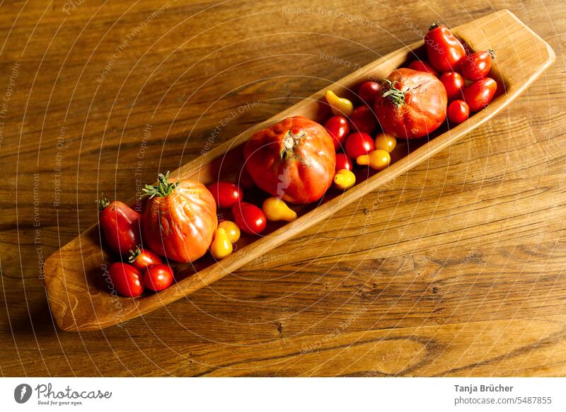 Rote und gelbe Tomaten von oben in einer länglichen Holzschale auf gemasertem Holztisch Gemüse rote Tomaten viele Tomaten erntefrisch frische Ernte