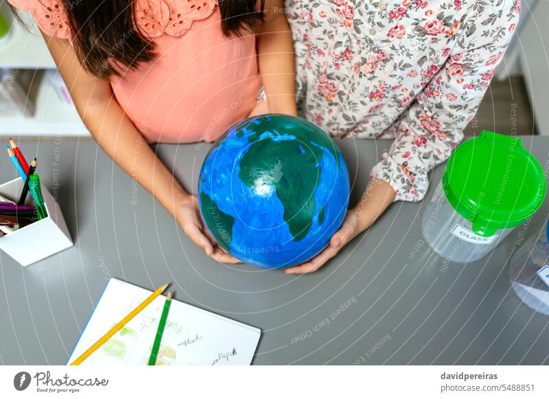 Zwei unkenntliche Studentinnen halten einen handgefertigten Globus der Erde Frau Schüler Beteiligung Welt Planet Hand wenig Mädchen Schule Bildung nachhaltig