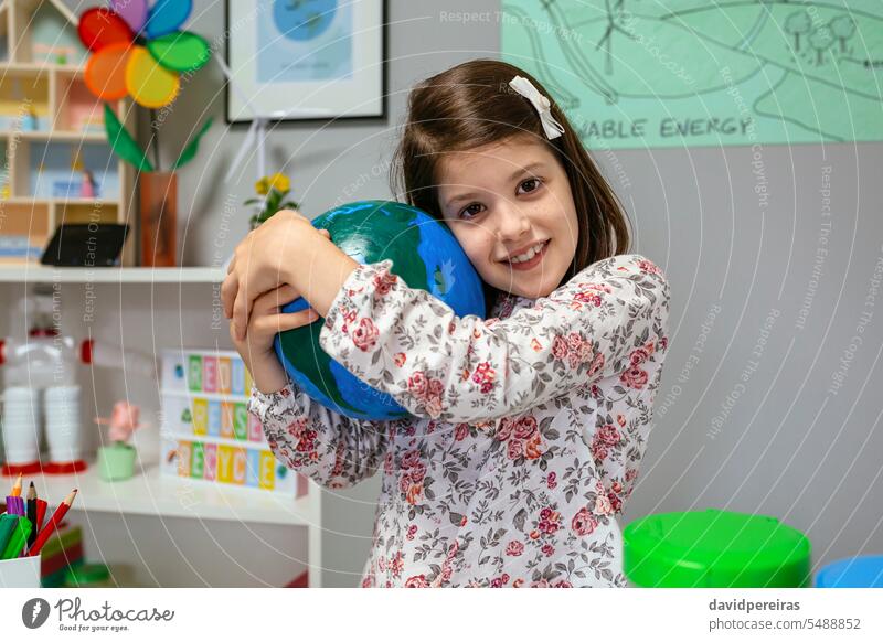 Eine Schülerin umarmt einen handgefertigten Globus im Ökologie-Klassenzimmer umarmend Welt Erde Planet Hand Frau Liebe wenig Mädchen Schule Lächeln lustig Glück